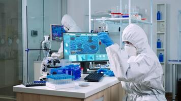 Chemist in coverall checking blood samples taking notes on computer in equipped laboratory. Team of doctors examining vaccine evolution using high tech researching diagnosis against covid19 virus photo