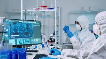 Chemist doctor in ppe suit working at pc while lab technician using microscope. Team of scientists examining vaccine evolution with high tech for researching treatment against covid19 virus photo