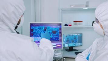 Scientists coworkers in coverall discussing about virus evolution in equipped laboratory pointing on computer desktop. Doctors examining vaccine evolution using high tech researching diagnosis photo