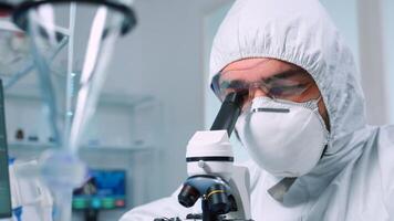 Biochemist in ppe suit looking through a microscope during experiment in sterile lab. Chemist researcher examining virus evolution using high tech for vaccine scientific research against covid19 photo