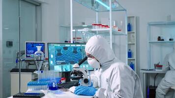 Scientist in ppe suit working in laboratory using modern microscope with slides. Team of chemists researcher examining virus evolution using high tech for vaccine scientific research against covid19 photo