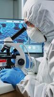 Scientist in protection suit looking through a microscope in equipped lab. Team of chemists examining virus evolution using high tech for scientific research of vaccine development against covid19. photo