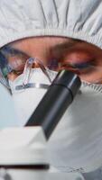 Close up of experienced biologist in ppe suit working on microscopes in equipped laboratory. Chemist in coverall examining vaccine evolution using high tech researching diagnosis against covid19 virus photo