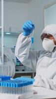 Biologist doctor in ppe suit checking liquid sample typing on pc in equipped laboratory. Team examining vaccine evolution in medical lab using high tech and chemistry tools for scientific research photo