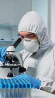 Medical research scientist in ppe suit conducting vaccine development using digital microscope in a biological applied science laboratory. Caucasian lab engineer in coverall working on medical treatment photo