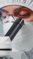 Portrait of lab technician with protection suit examining samples using microscope in equipped laboratory. Scientist working with various bacteria, tissue and blood samples for pharmaceutical research photo
