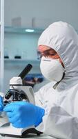 Scientist in ppe suit placing a slide on specimen stage of a laboratory microscope making adjustments. Chemist in coverall working with various bacteria, tissue blood samples for antibiotics research photo