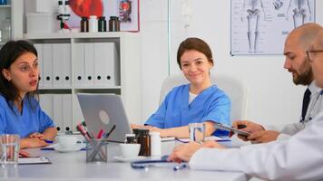 Woman assistent typing on laptop at desk looking at camera and smiling in busy workday in modern medical office. Woman specialist writing on notepad during brainstorming in meeting room photo