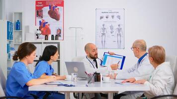 Doctor is brainstorming to analyze medical problems pointing on clipboard showing to colleagues medical statistics. Coworkers working in hospital office discussing symptoms of disease, taking notes. photo