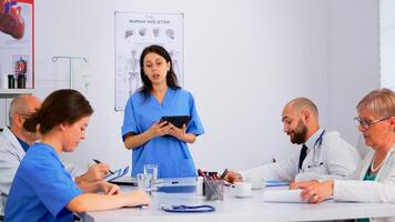 Medical people meeting and planning with shareholders in hospital office sitting at desk. Doctors and nurses brainstorm ideas together, physicians diagnosis and presentation data using tablet photo