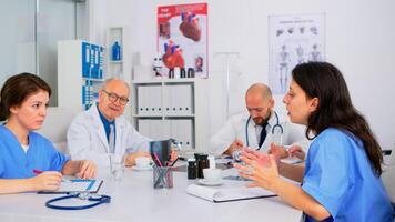 Team of physicians talking about symptoms of disease in clinic room during brainstorming sitting in hospital meeting room. Medic discussing about medicine at medical conference solving health problems photo
