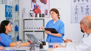 Team of doctors discussing diagnosis sitting at table in clinic, nurse holding clipboard sharing tasks to colleagues. Group of physicians talking about symptoms of disease in clinic office photo