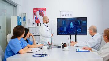 Man doctor presenting human internal structure in front of attantive colleagues using digital monitor in hospital meeting office during brainstorming. Medical team analysing diagnosis of patients photo