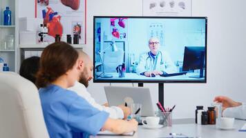 Concentrated purposeful experienced medical team holding online meeting with senior doctor on interactive screen. Team of specialists discussing diagnosis of patients uing conference photo