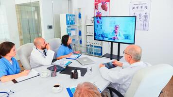 Team of medical staff during conference with doctor in hospital meeting room. Medicine staff using internet during online meeting with expert doctor for expertise, nurse taking notes. photo