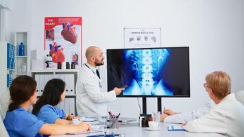 Cvalified head doctor in white coat sitting in hospital boardroom explaining spin functions pointing on digital x-ray image. discussing symptoms of disease for further treatment photo