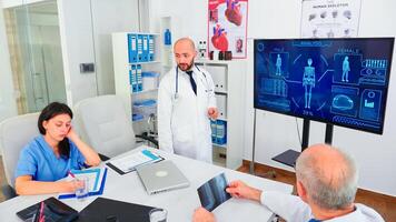 Medical expert talking about healthcare during seminar with hospital staff in conference room pointing at digital monitor. Clinic herapist discussing with colleagues about disease, medicine professional photo