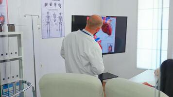 Experienced man doctor discussing about heart issues using digital image, together with cvalified colleagues in meeting room, pointing on monitor. Doctors analysing diagnosis for treatment of patients photo