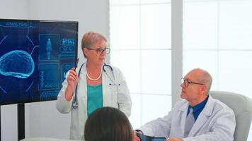 Neurologist reading brain waves on monitor while doctor is wearing headset with sensors. Monitor shows modern brain study while team of scientist adjusts the device working in hospital conference room photo