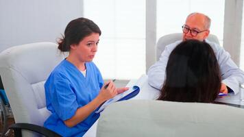 Young medical assistant briefing staff of doctors about patient diagnosis in conference room using clipboard. Clinic expert therapist talking with colleagues about disease, medicine professional photo