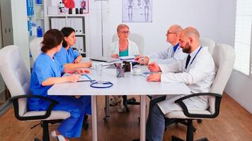 Medical women practitoner writing notes on clipboard wearing blue uniform during conference with coworkers. Clinic expert therapist talking with colleagues about disease, medicine professional. photo