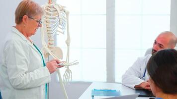 Female radiologist doctor holding presentation using skeleton in front of medical staff. Clinic expert therapist talking with colleagues about disease, medicine professional working in boardroom photo