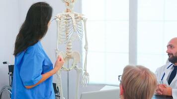 Female nurse demonstrating on skeleton in front of medical surgeons in conference room. Clinic expert therapist talking with colleagues about disease, medicine professional photo