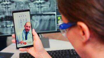 Close up of nurse talking on call with specialist stomatologist using mobile phone sitting in modern dental clinic in front of pc with digital x-ray. Dentistry doctor explaining patient symptoms photo