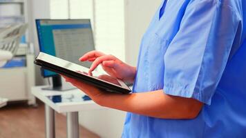 Close up of assistant holding tablet and analysing teeth digital radiography of patient standing in stomatologic clinic, while doctor is working in background. Nurse using modern technology photo