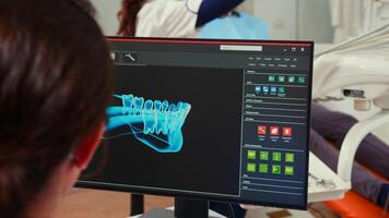 Stomatologist nurse looking at digital dental fingerprint on computer sitting in stomatological clinic while dentistry doctor is working with patient in background examining teeth problems. photo