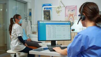 Stomatologist nurse talking with patients using headset making dental appointments sitting in front on computer while doctor is working with patient background examining teeth problem photo