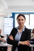 Woman entrepreneur smiling at camera standing in conference room, preparing for meeting with partners. Manager working in professional start up financial business, modern company workplace ready for meeting. photo