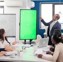 Leader of company presenting financial plan using mockup display in front of diverse team brainstorming. Manager explainig project strategy on green screen monitor with chroma key desktop in boardroom photo