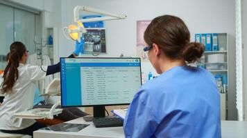 Orthodontist assistant taking notes on clipboard, checking appointments, while specialist dentist doctor with face mask examining patient with toothache sitting on stomatological chair. photo