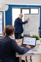 Confident man business coach giving flipchart presentation training diverse workers group at workshop, Serious speaker boss executive, business trainer explaining development strategy to motivated mixed race employees. photo