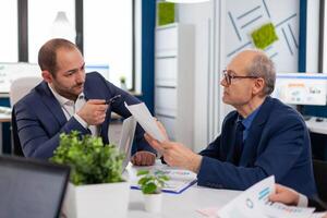 Senior entrepreneur discussing with coworker holding documents in conference during briefing Businessman discussing ideas with colleagues about financial strategy for new start up company. photo