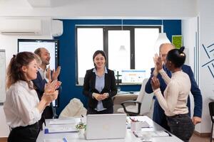 Happy overjoyed financial startup team standing clapping a in conference briefing. Multiethnical partners coworkers celebrate successful teamwork result at company briefing photo
