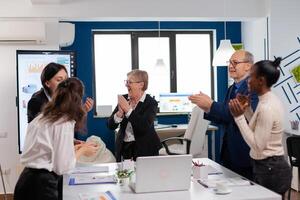 Victorious overjoyed diverse team of businesspeople clapping together in conference room. Multiethnical partners coworkers celebrate successful teamwork result at company briefing photo