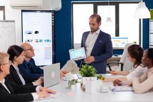 Succesful business man presenting the good evolution of company using digital tablet. Project leader discussing with teamworkers in broadroom, analysing charts, graphs, financial evolution of company. photo