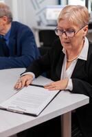 Woman reading financial documents in conference room before signing it. Executive director meeting shareholders in start up office, making satisfactorily agreement. photo