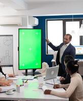 Leader of company presenting financial plan using mockup display in front of diverse team brainstorming. Manager explainig project strategy on green screen monitor with chroma key desktop in boardroom photo