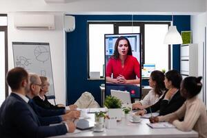 Diverse team of coworkers talking with project manager using webcam during business conference sitting in broadroom. Business people talking to webcam, do online conference participate internet brainstorming, distance office discussion photo