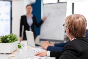 Leader making sales report for top company managers drawing charts on white board. Serious speaker boss executive, business trainer explaining development strategy to motivated mixed race employees. photo