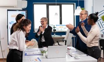 Victorious overjoyed diverse team of businesspeople clapping together in conference room. Multiethnical partners coworkers celebrate successful teamwork result at company briefing photo