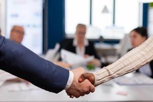 Close up of multiracial business partners standing in front of conference desk shaking hands after signing partnership contract. Diverse team being happy for successful negotiations in startup company photo
