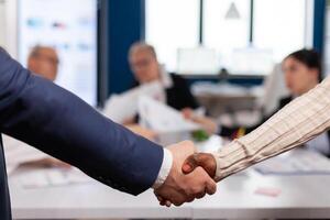 Close up of multiracial business partners standing in front of conference desk shaking hands after signing partnership contract. Diverse team being happy for successful negotiations in startup company photo