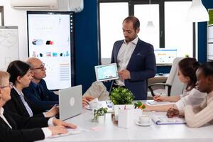 Succesful business man presenting the good evolution of company using digital tablet. Project leader discussing with teamworkers in broadroom, analysing charts, graphs, financial evolution of company. photo