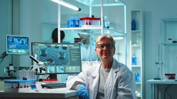 Portrait of senior scientist woman looking exhausted at camera sitting in equipped lab late at night. Team examining virus evolution using high tech for scientific research, vaccine development photo