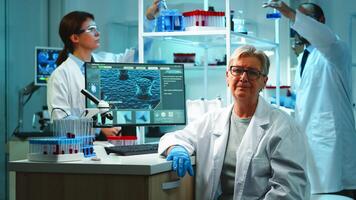 Portrait of old chemist woman with fatigued face in front of camera in equipped lab late at night. Team examining virus evolution using high tech and chemistry tools for research, vaccine development photo