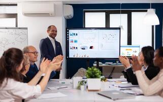 Succesful business man presenting the good evolution of company using digital device. Diverse multiethnic colleagues with new opportunity enjoing victory meeting in broadroom office. photo